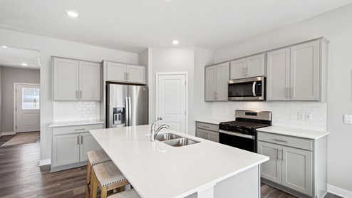 Angled view of kitchen with gray cabinetry and quartz countertops.
