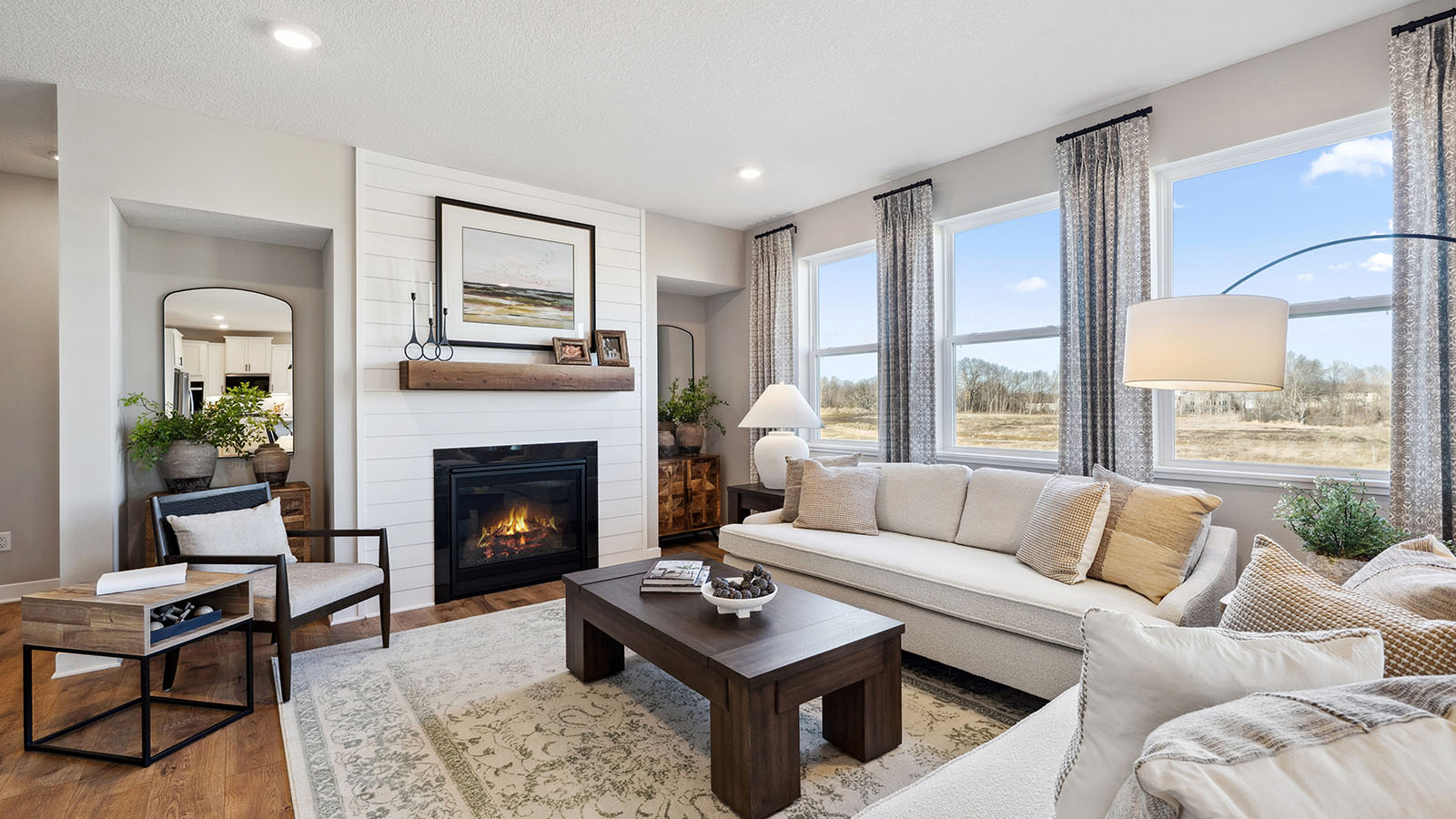 .Spacious living room with brown flooring, white walls, a black fireplace and windows