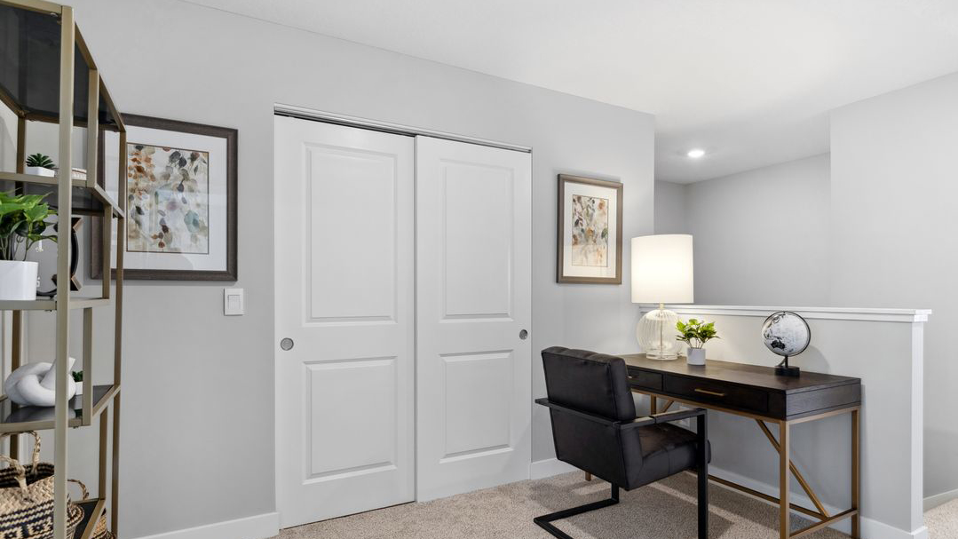 Upper level carpeted loft area staged with desk and armchair.