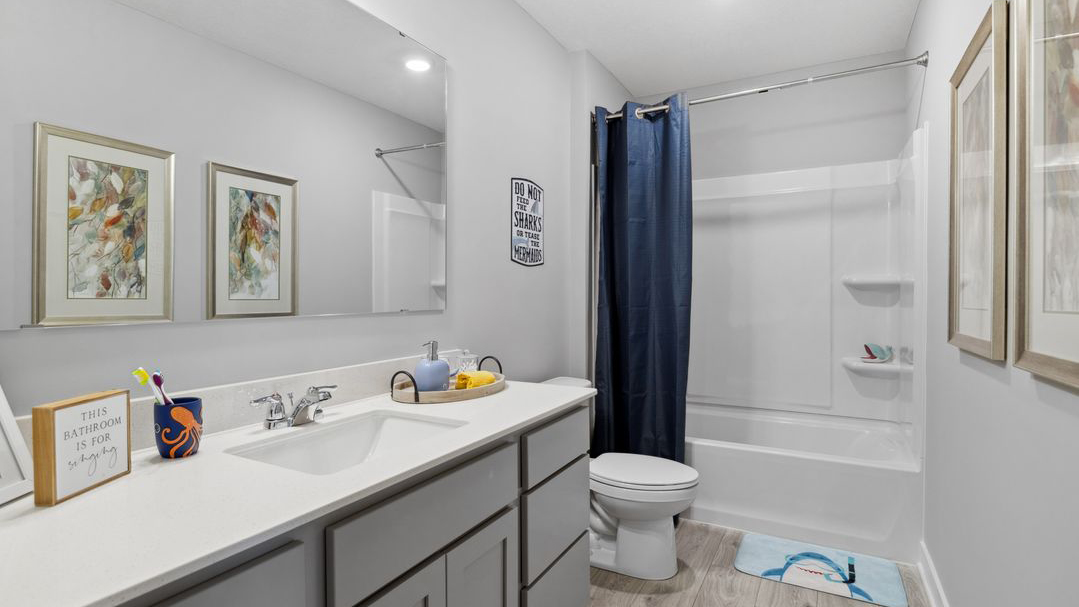 Secondary full bathroom with gray single sink vanity and quartz vanity countertop.