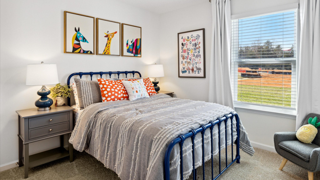 Bedroom showing a made bed, art on walls and large windows.