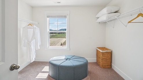 Interior large primary walk-in closet with window and ottoman