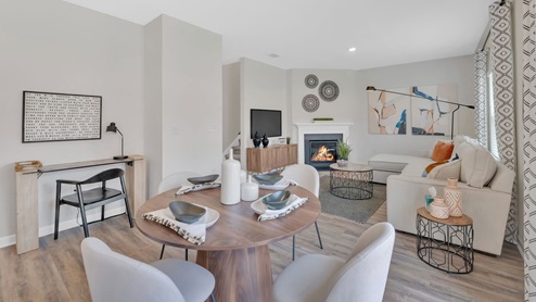 An large living area with light wood flooring, neutral-colored walls, and a ceiling fan with lights in the center of the room.