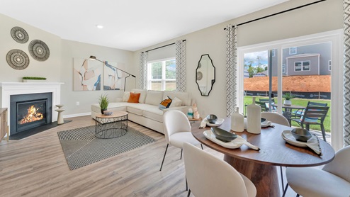 An open living area with light wood flooring, neutral-colored walls, and large windows that open into the back patio.