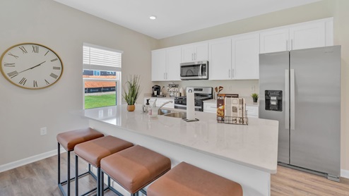 A spacious, modern kitchen with white cabinets and light granite countertops, featuring a large central island with a double sink and silver faucet.
