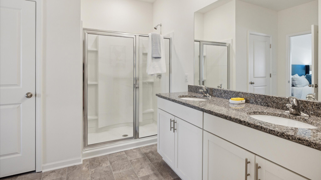 Primary bathroom with a double-sink vanity, large mirrors, and a spacious glass-enclosed walk-in shower, featuring light tile flooring and white cabinetry.