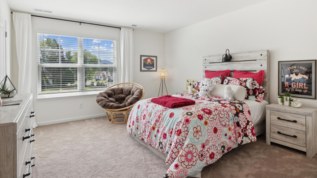 Bright and cheerful bedroom featuring a floral comforter set, rustic wood headboard, matching nightstand and dresser, cozy papasan chair by a large window, and playful decor with girly accents.