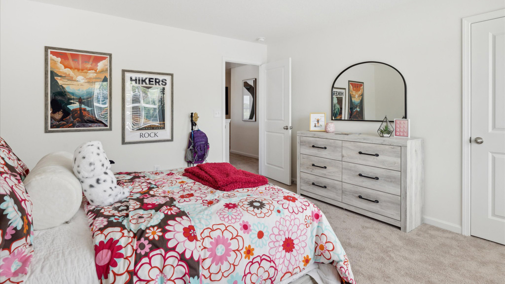 Youthful bedroom with a floral bedspread, plush pillows, a rustic light wood dresser with a curved mirror, and hiking-themed wall art adding a fun, adventurous touch.