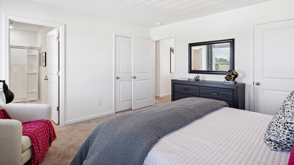 Contemporary bedroom with a charcoal-gray dresser and matching mirror, neutral walls and carpet, and a view into an ensuite bathroom featuring a glass-enclosed shower.