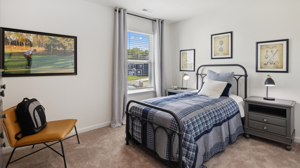 A cozy bedroom featuring a twin bed with a plaid comforter, golf-themed wall art, and a large window letting in natural light.