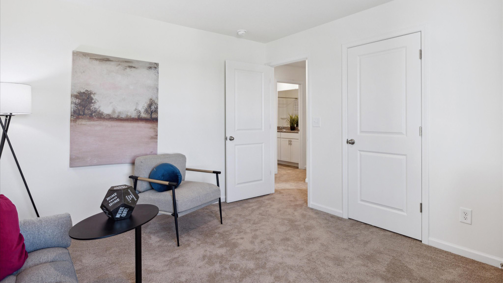 A cozy carpeted room with minimal furnishings, soft lighting, and access to an adjoining bathroom—perfect as a private bedroom or adaptable flex space.