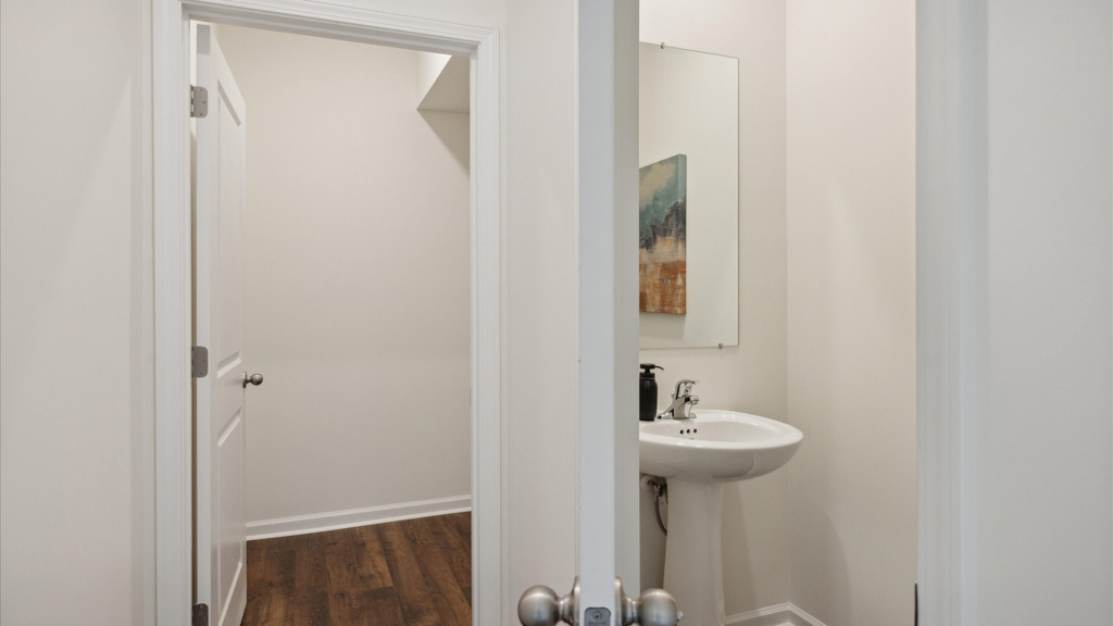 Compact half bathroom with a pedestal sink, large mirror, neutral walls, and wood-style flooring, viewed through an open double doorway.