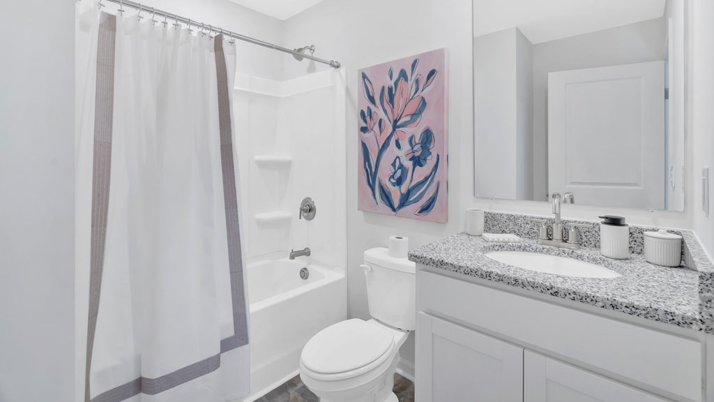 Bathroom with speckled countertops, white cabinets, toilet and full shower and tub with white curtain.
