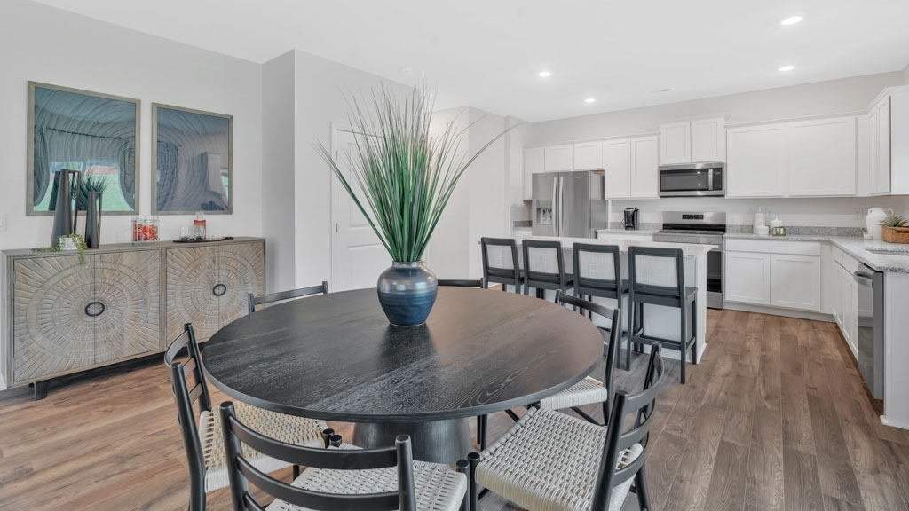 Open kitchen and dining area featuring a round black dining table with six chairs, a large kitchen island with barstool seating, white cabinetry, stainless steel appliances, and wood-style flooring.