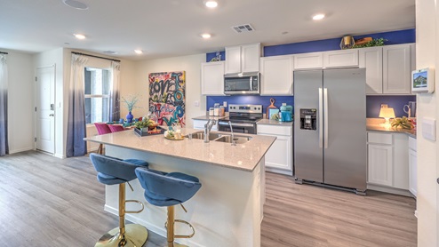 Our 1410 model kitchen in the Kalea Trails Community with white shaker cabinets, quartz countertops, a kitchen island/seating area, and Whirlpool Stainless Steel appliances.
