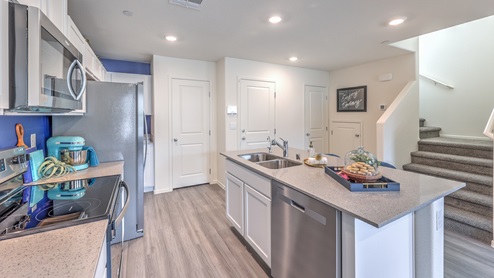 Our 1410 model kitchen in the Kalea Trails Community with white shaker cabinets, quartz countertops, a kitchen island/seating area, and Whirlpool Stainless Steel appliances.
