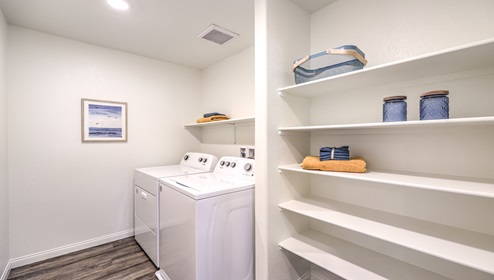 Our Cambria Bay 1865 model laundry room with shelves and a washer and dryer.