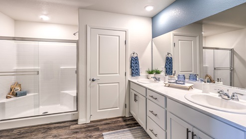 Attached to the Bedroom One Suite, our 1865 model bathroom with granite countertops at the double Bath Vanity, a walk-in shower, mirror, and grey cabinets.
