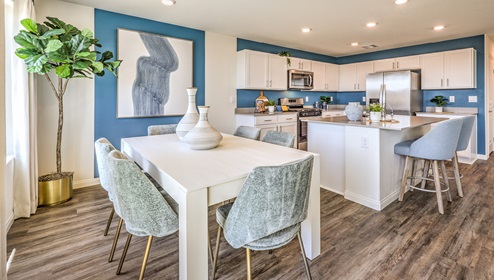 The Cambria Bay 1865 model Dining Room adjacent to the kitchen with a table and window.