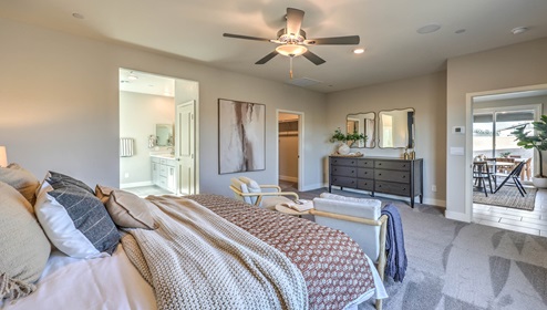 The Bedroom One Suite in our Symmetry Manor 2754 model with carpet flooring, large windows, a walk-in closet, and a ceiling fan with a light kit.
