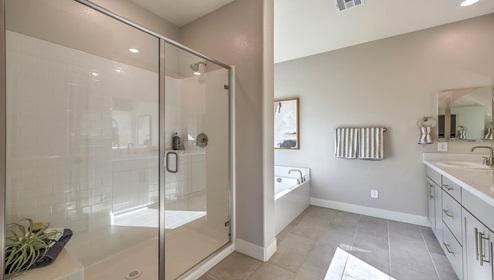 Attached to the Bedroom One Suite, our 2754 model bathroom with granite countertops at the double Bath Vanity, a walk-in shower, bath tub, mirror, and brown cabinets.