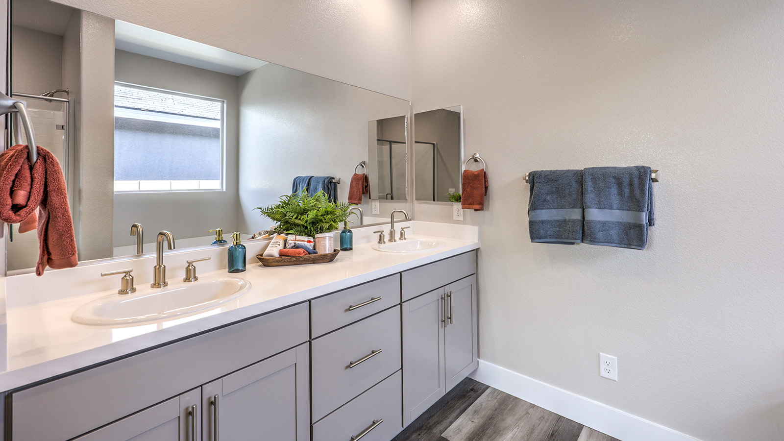 Attached to the Bedroom One Suite, our 2754 model bathroom with granite countertops at the double Bath Vanity, a walk-in shower, bath tub, mirror, and brown cabinets.
