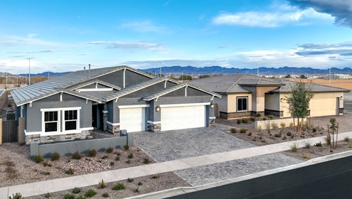 Our 2754 model home in the Heartland Manor community withgrey and whoite exterior paint schemes, a flat tile roof, front yard landscaping, paver walkways, and a three-car garage.