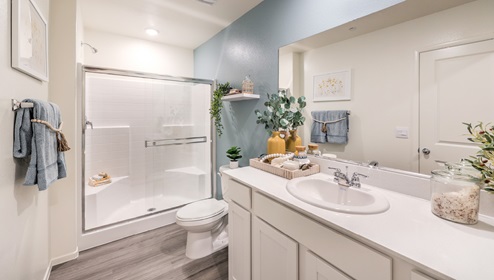 Attached to the Bedroom One Suite, our 1410 model bathroom with quartz/marble fusion countertops at the Bath Vanity, a walk-in closet, mirror, and white cabinets.