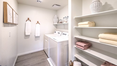 Our Symmetry Bay 1865 model laundry room with shelves and a washer and dryer.