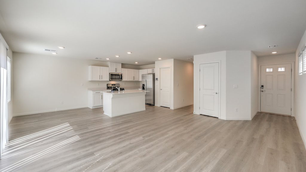 The Symmetry Bay 1715 Plan open concept Great Room with LVP panel flooring, large windows, and a sliding door to the backyard.