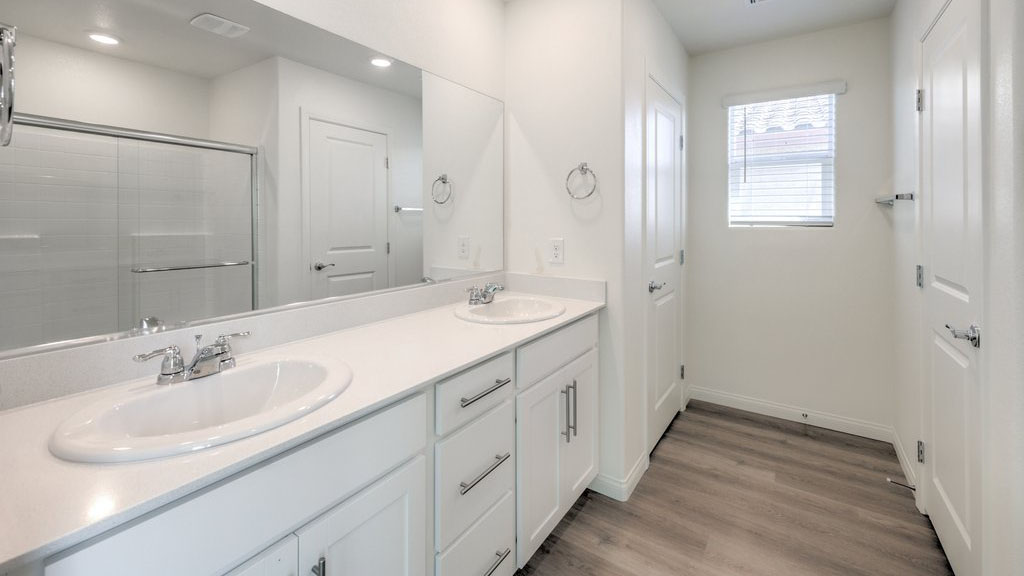 Attached to the Bedroom One Suite, our 1715 model bathroom with granite countertops at the double Bath Vanity, a walk-in shower, mirror, and white cabinets.