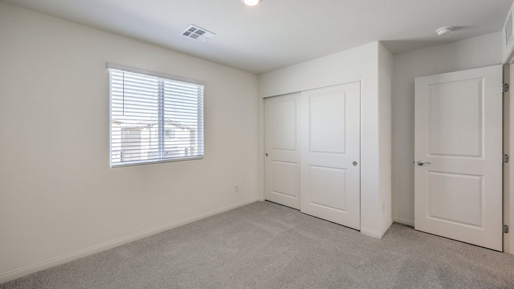 The Bedroom Three option in our Symmetry Bay 1715 model with carpet flooring, a sliding closet, and a window, furnished with a desk and chair.