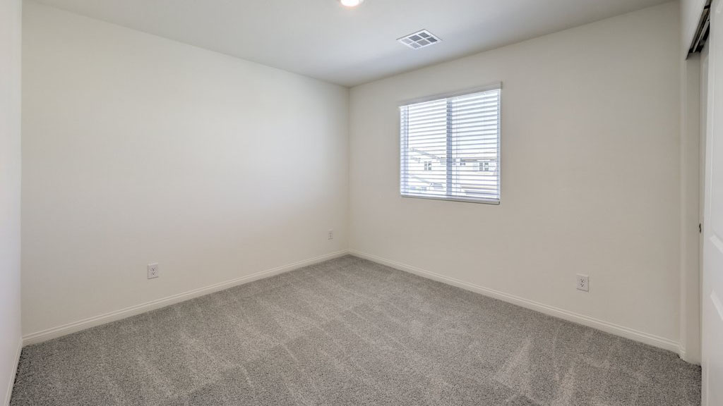 The Bedroom Three option in our Symmetry Bay 1715 model with carpet flooring, a sliding closet, and a window, furnished with a desk and chair.