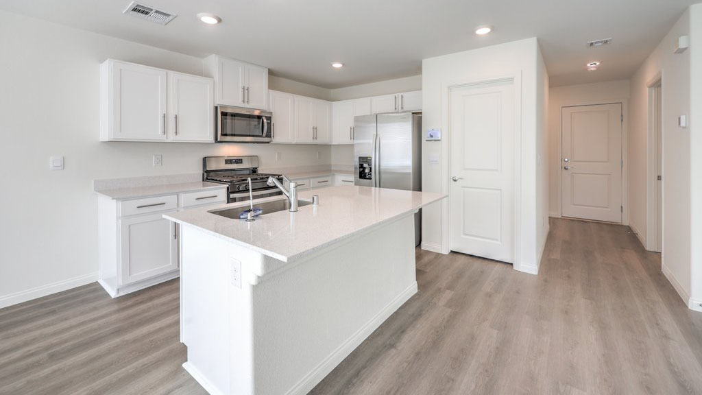 Our 1715 model kitchen in the Heartland Bay Community with white shaker style cabinets, granite slab countertops, a kitchen island, large pantry, and Whirlpool Stainless Steel appliances.