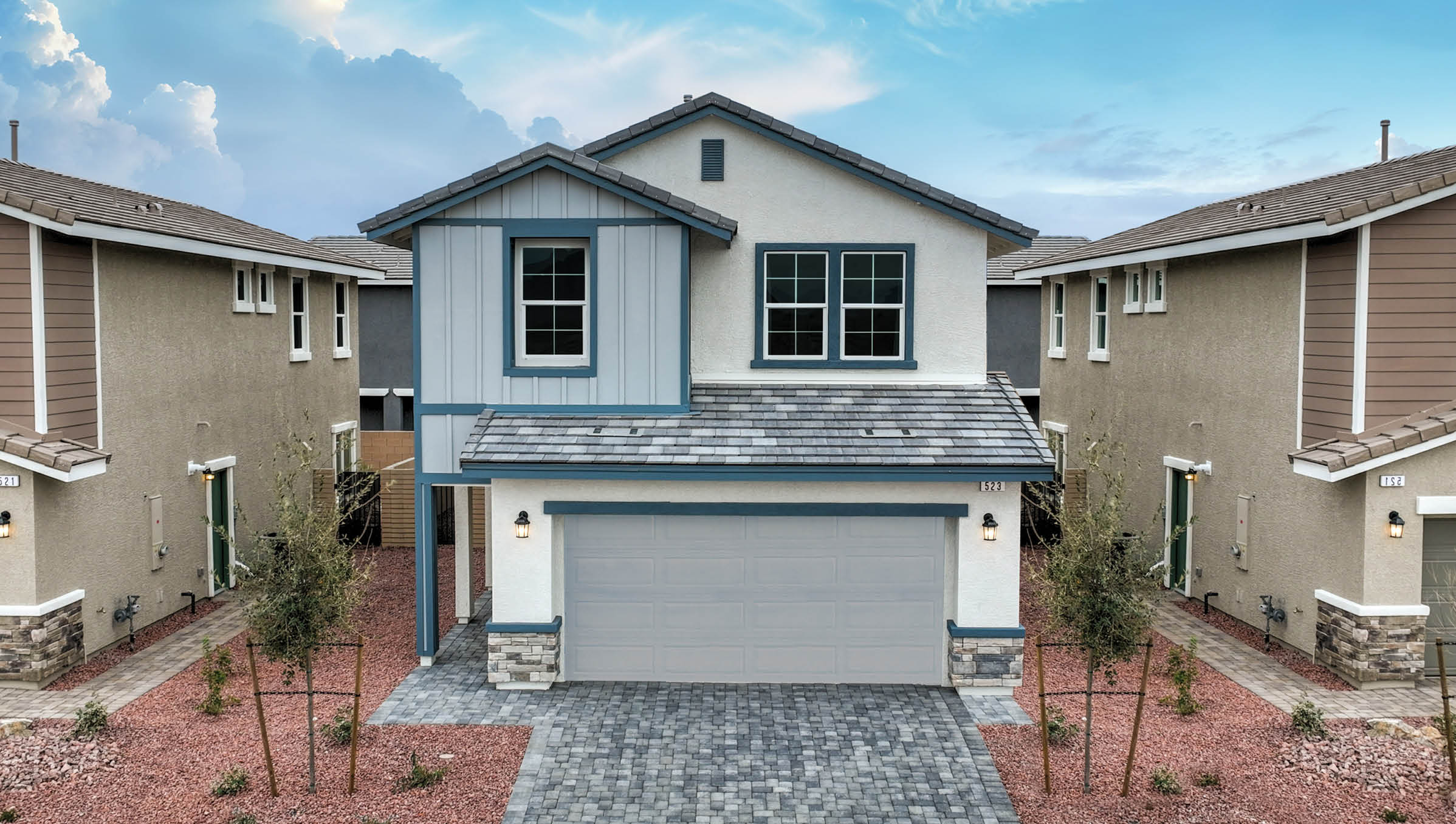 Our 1802 Plan home features a modern farmhouse design with a white stucco and gray board-and-batten exterior. It includes a gray two-car garage, stone veneer accents, and a coordinating gray flat tile roof. The front yard is designed with drought-resistant landscaping, featuring decorative rocks and native plants for a stylish, low-maintenance appeal.