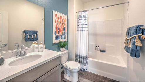 The Symmetry Falls 3000 Model Second Bathroom featuring Luxury Vinyl Plank flooring, a quartz countertop with an undermount sink, and a combination tub and shower with white tile surround. The bathroom includes built-in storage, modern fixtures, and is conveniently located near the secondary bedrooms for easy access.