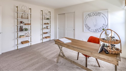 The Symmetry Falls 3000 Model Fifth Bedroom, shown as a home office, features wall-to-wall carpet, a large window for natural light, and a spacious layout with a sliding-door closet. This flexible room can be used as a private office, guest room, or additional bedroom, offering both functionality and quiet separation from the main living areas.