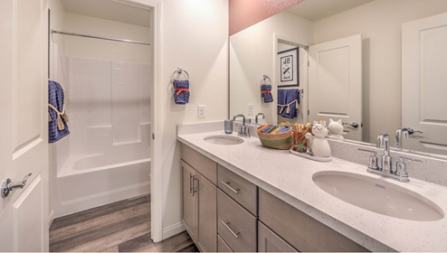 The Symmetry Falls 3000 Model Third Bathroom featuring Luxury Vinyl Plank flooring, dual sinks with quartz countertops, and a separate area with a combination tub and shower surrounded by white tile. This well-appointed bathroom offers functionality and privacy, conveniently serving the upstairs bedrooms and loft area.