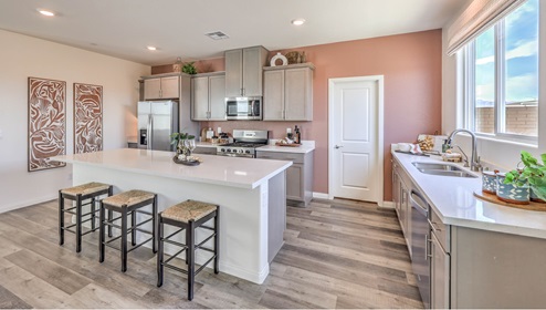 The Symmetry Falls 3000 Model Kitchen with Luxury Vinyl Plank flooring, featuring Whirlpool stainless steel appliances, a quartz countertop with a 4” backsplash, and a large center island with seating. The kitchen includes ample cabinetry, a walk-in pantry, and expansive windows that bring in natural light for a bright and functional cooking space.
