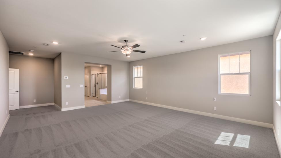 The Bedroom One Suite in our Symmetry Summit 3825 model with carpet flooring, large windows, and a ceiling fan with a light kit.