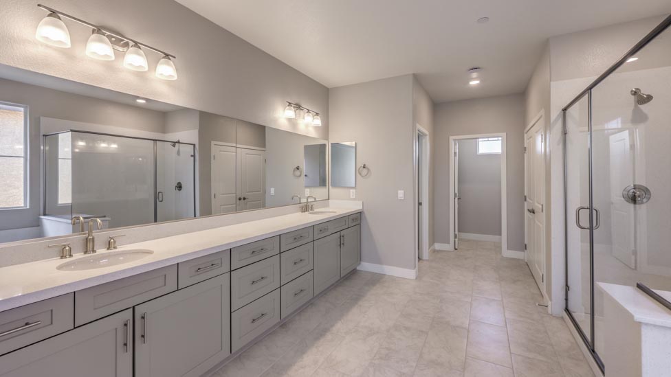 Attached to the Bedroom One Suite, our 3825 model bathroom with quartz countertops at the double Bath Vanity, a walk-in closet, mirror, and grey cabinets.