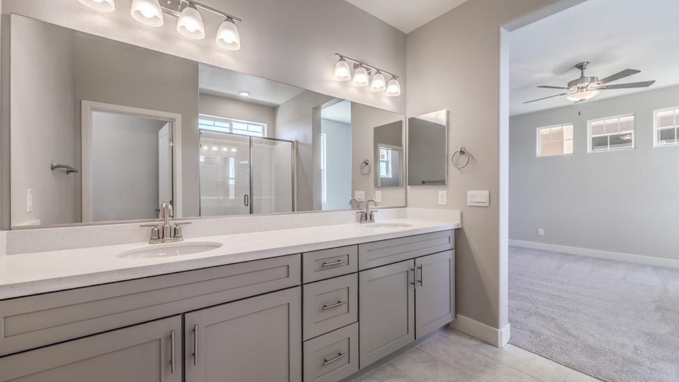 Attached to Bedroom Five, 3825 model Bathroom Three with quartz countertops at the double Bath Vanity, a walk-in shower, mirror, and grey cabinets.