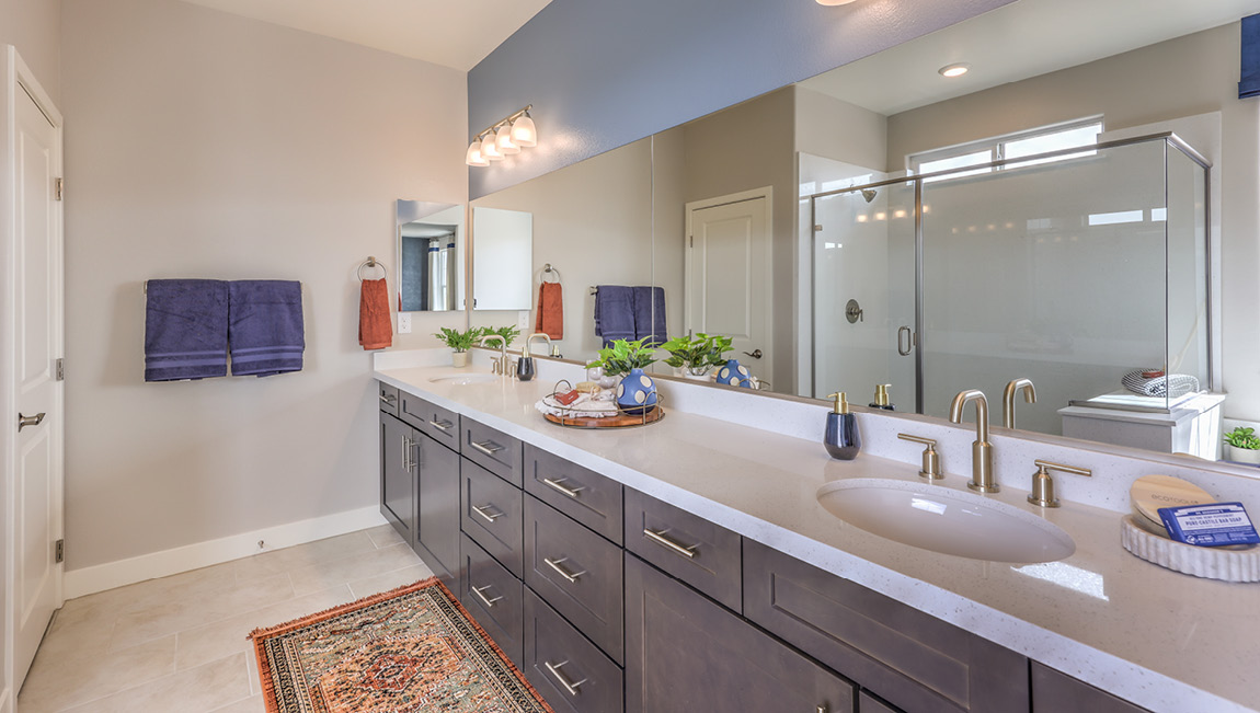 Attached to the Bedroom One Suite, our 4425 model bathroom with granite countertops at the double Bath Vanity, a walk-in closet, mirror, and brown cabinets.