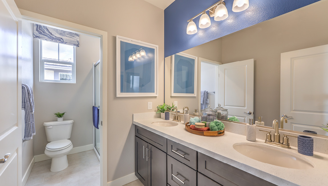 Bathroom Two in our Symmetry Summit 4425 model with granite countertops at the double Bath Vanity, a walk-in shower, mirror, and brown cabinets.
