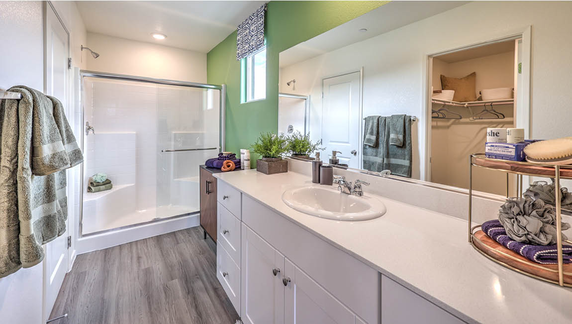 Attached to the Bedroom One Suite, our 1171 model bathroom with quartz/marble fusion countertops at the Bath Vanity, a walk-in shower, walk-in closet, mirror, and white cabinets.