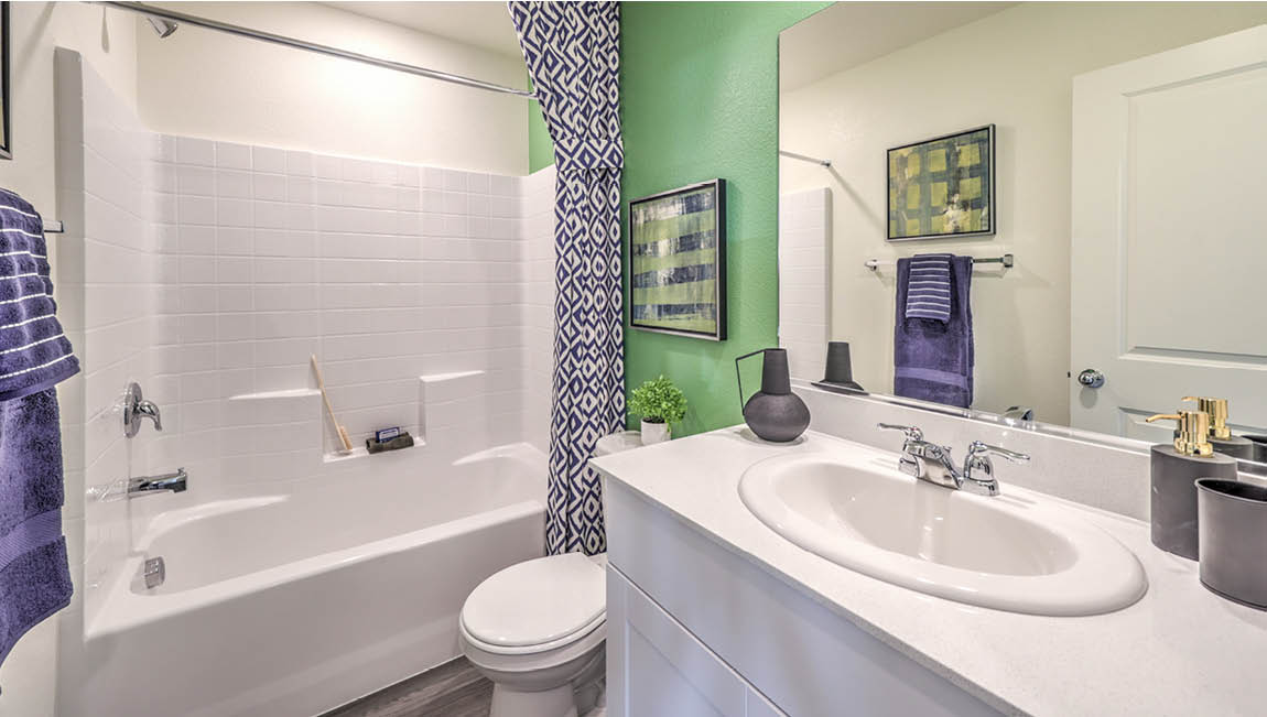 Bathroom Two in our Juno Pointe 1171 model with quartz/marble fusion countertops at the Bath Vanity, a walk-in shower, mirror, and white cabinets.