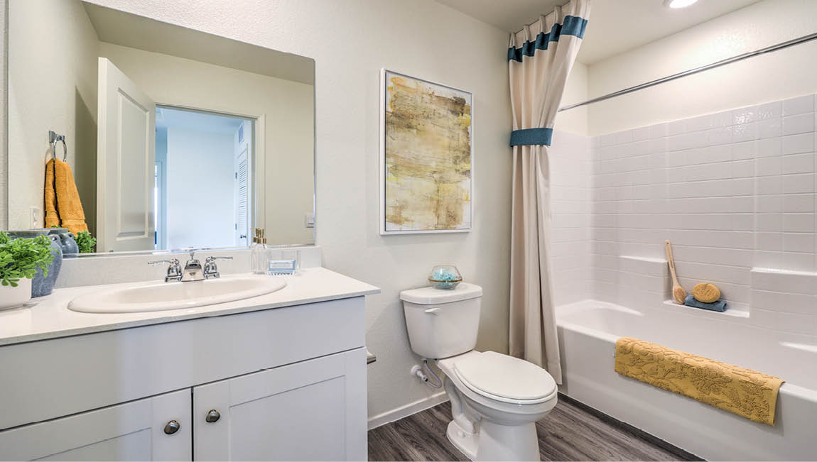 Bathroom Two in our Juno Pointe 1349 model with quartz/marble fusion countertops at the Bath Vanity, a walk-in shower, mirror, and white cabinets.