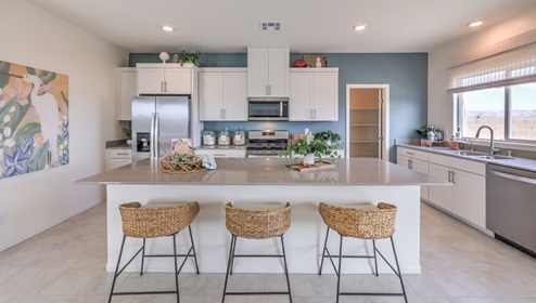 Our 3000 model kitchen in the Heartland Falls Community with white shaker style cabinets, Granite Slab countertops, a kitchen island, window, and Whirlpool Stainless Steel appliances.