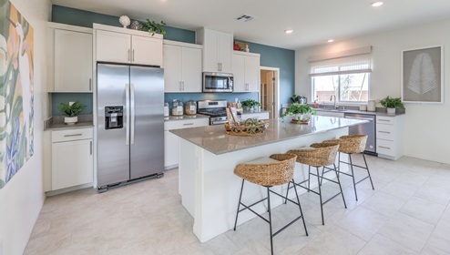 Our 3000 model kitchen in the Heartland Falls Community with white shaker style cabinets, Granite Slab countertops, a kitchen island, window, and Whirlpool Stainless Steel appliances.