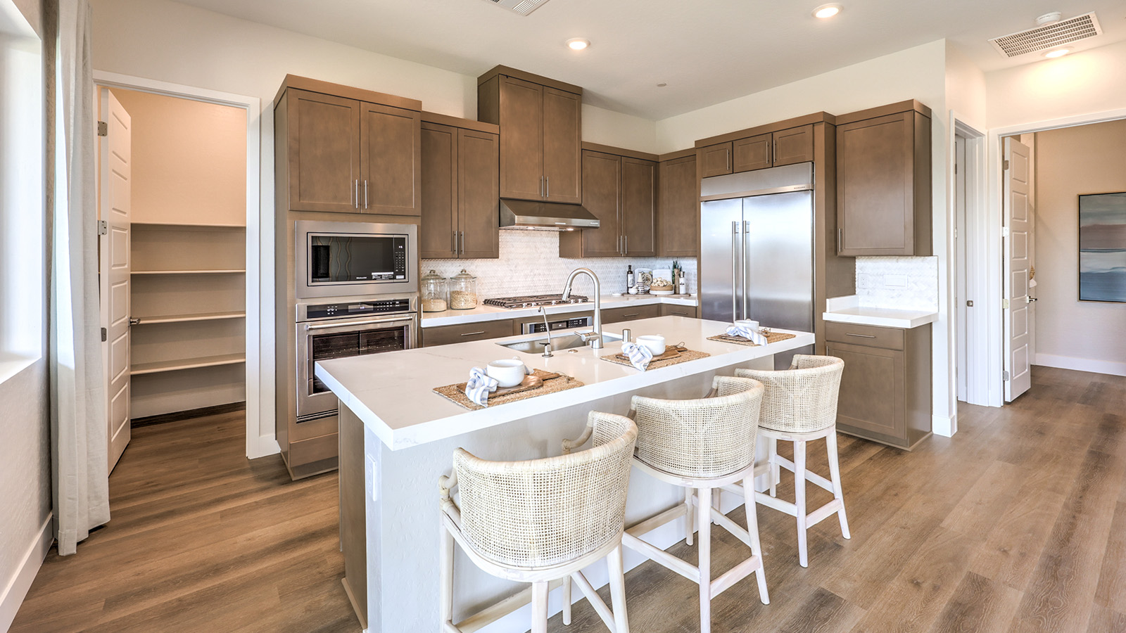 Our 3765 model kitchen in the Heartland Summit Community with white shaker style cabinets, granite countertops, a kitchen island, 5-burner cooktop, large pantry, and Whirlpool Stainless Steel appliances.